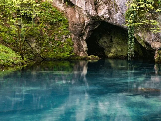 Ein ruhiger blauer Pool liegt am Eingang einer moosbewachsenen Höhle.