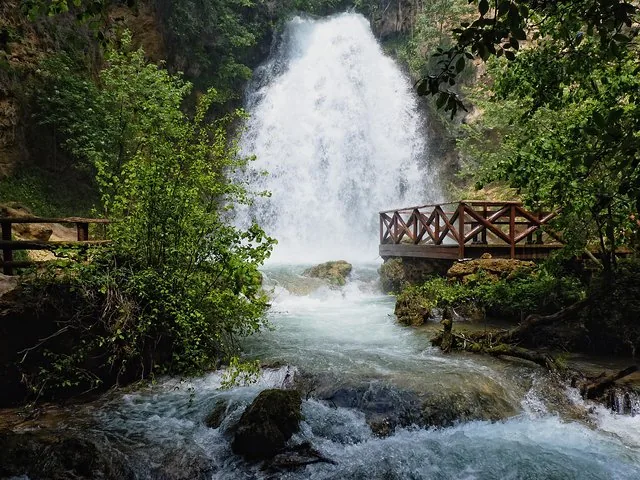 Ein rauschender Wasserfall stürzt neben einer hölzernen Aussichtsplattform in einen felsigen Bach.