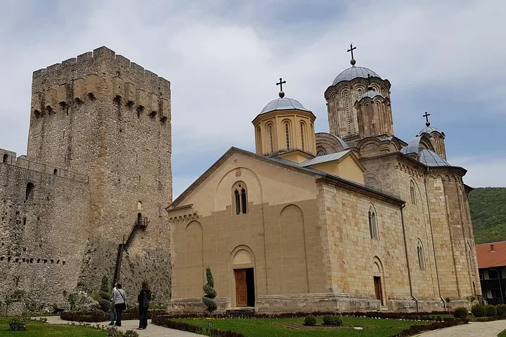 Une ancienne église en pierre aux toits en dôme se dresse à côté d'une haute tour médiévale.