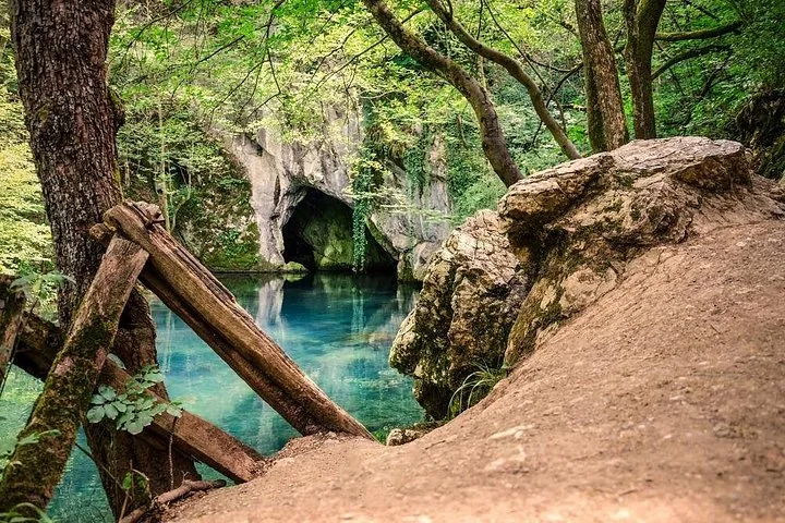 Vue sur un bassin bleu et l'entrée de la grotte depuis un sentier rocheux.