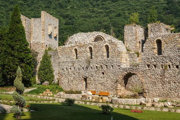Ruinen einer alten Steinburg oder eines Klosters mit grünen Hügeln im Hintergrund.